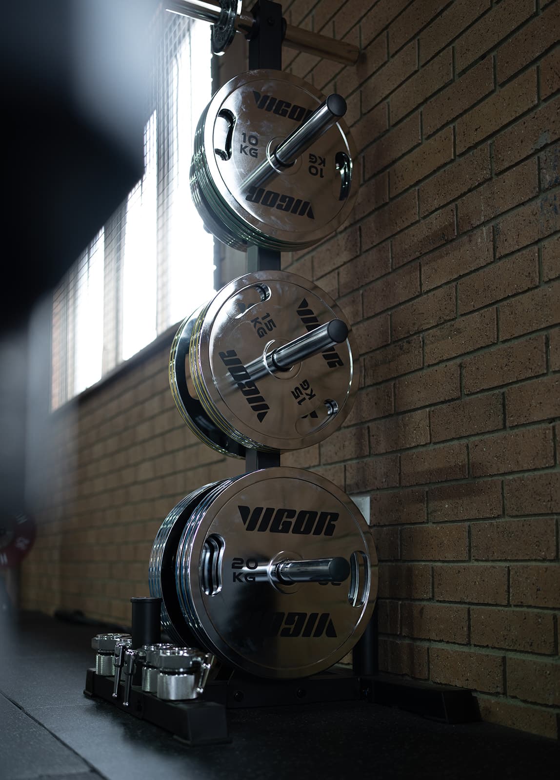 Polished Vigor weight plates stored on a rack beside the gym's brick wall